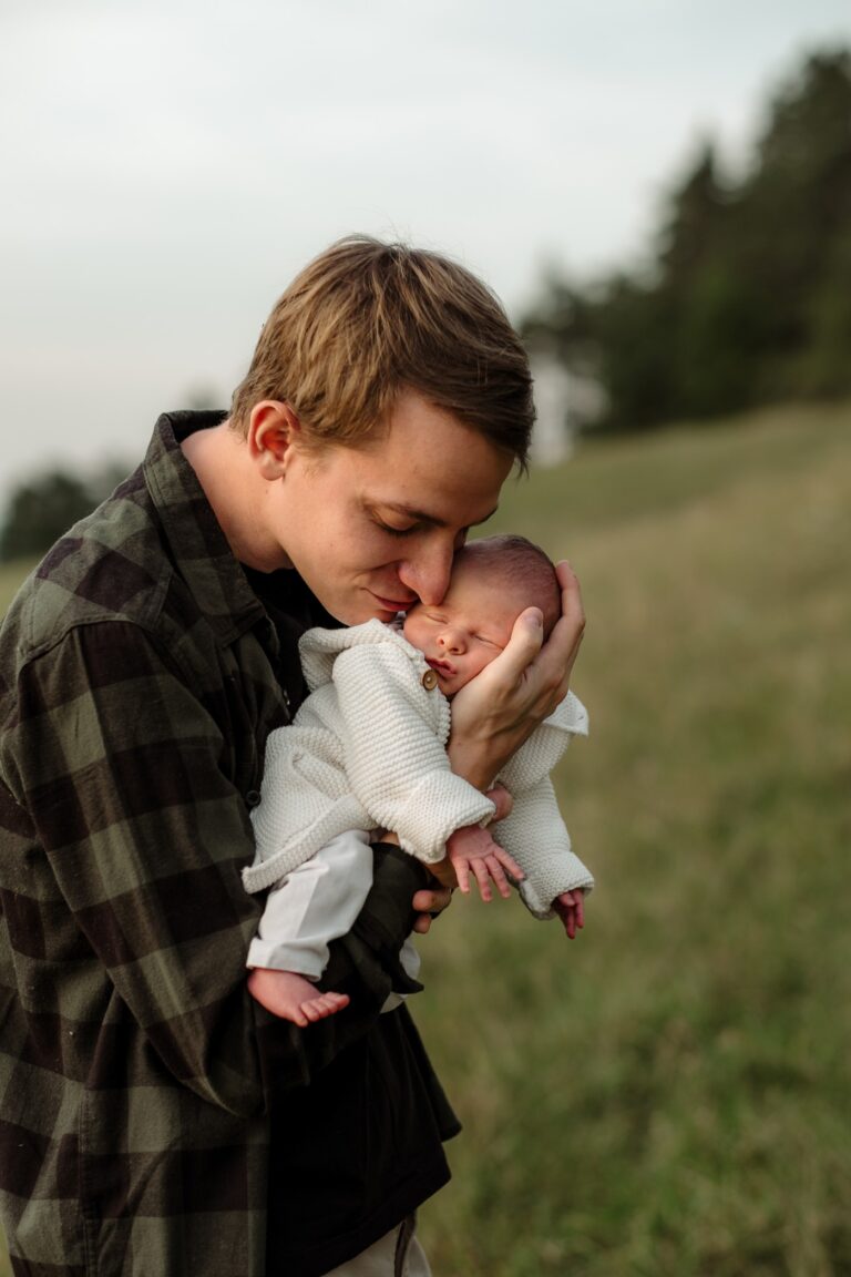 Tatínek dává pusinku miminku během newborn focení venku Praha