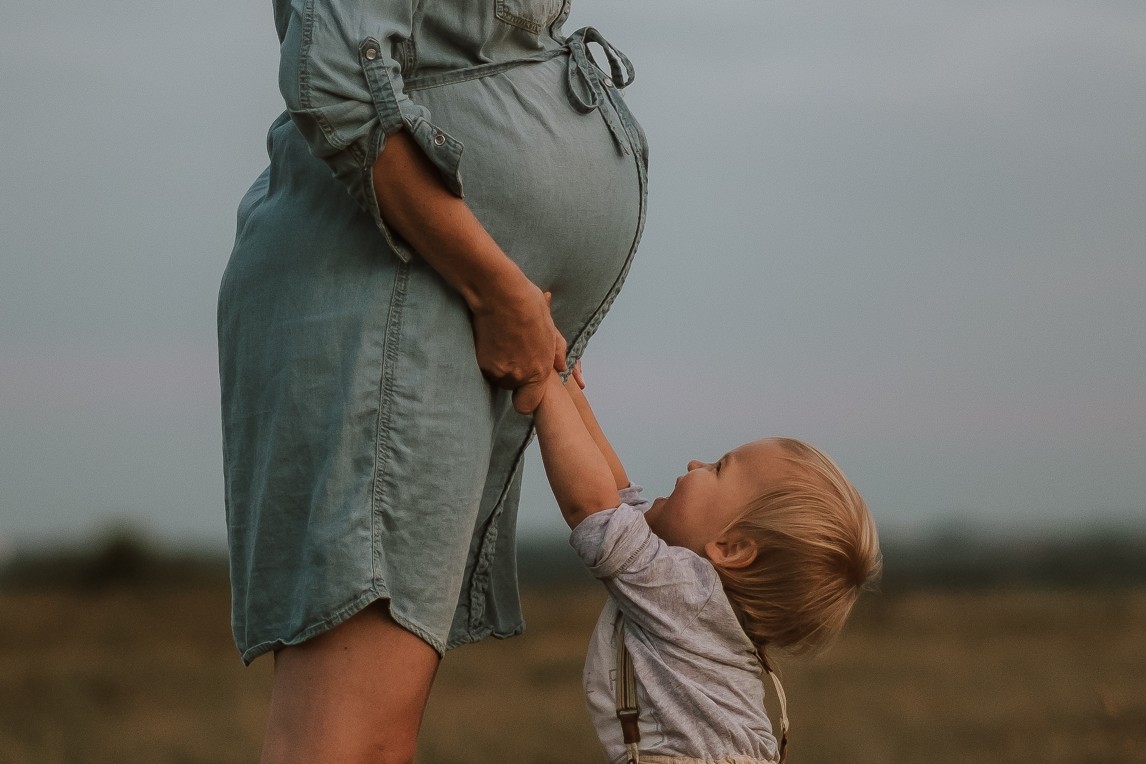 Malý bráška těšící se na miminko šahá na bříško maminky během těhotenského focení s dětmi.