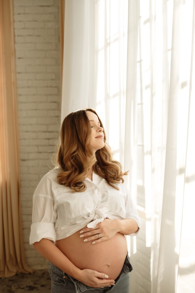 Žena si se zavřenými oči užívá těhotenské focení v ateliéru Praha