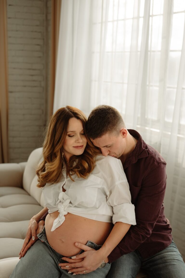 Nastávající rodiče se objímají a pusinkují při těhotenském focení v ateliéru Praha