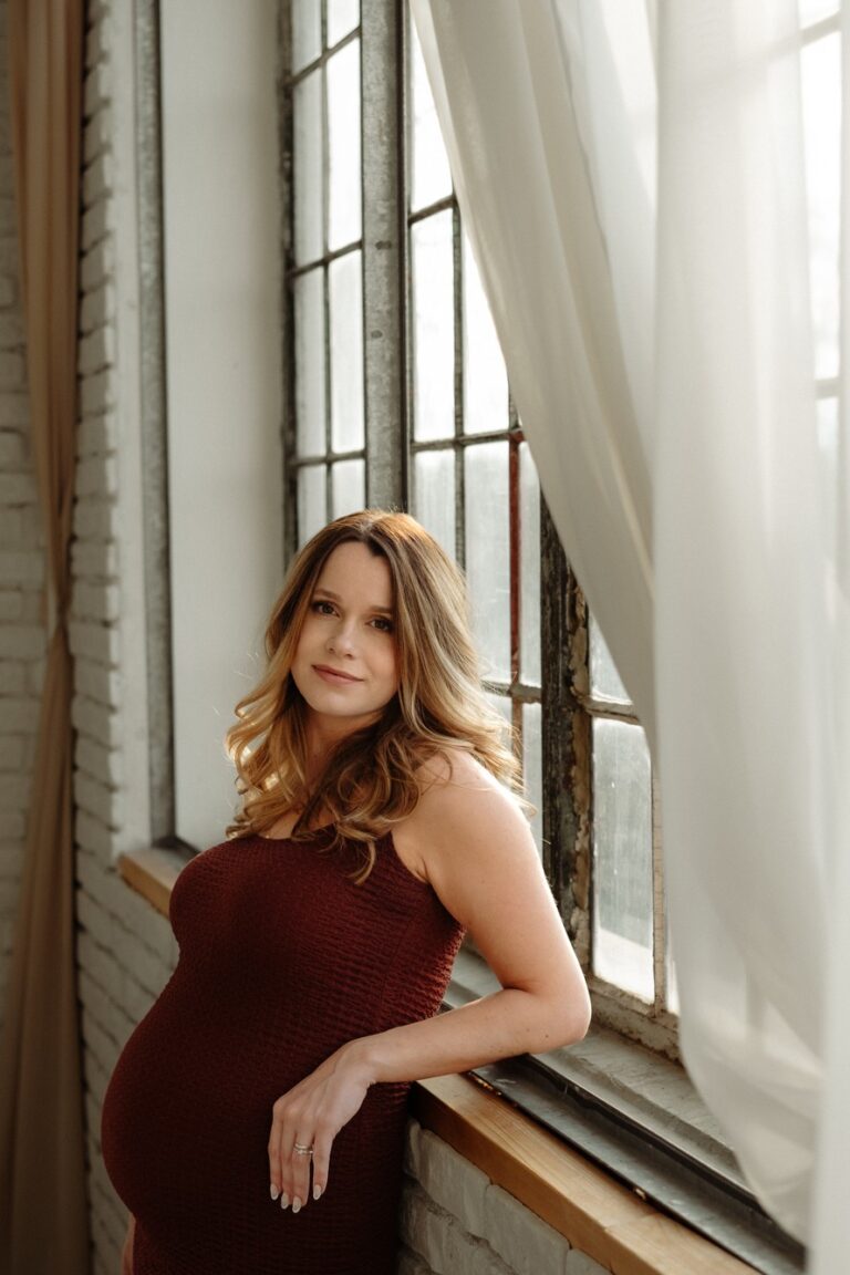 Těhotná žena stojí u okna při těhotenském focení v ateliéru Praha